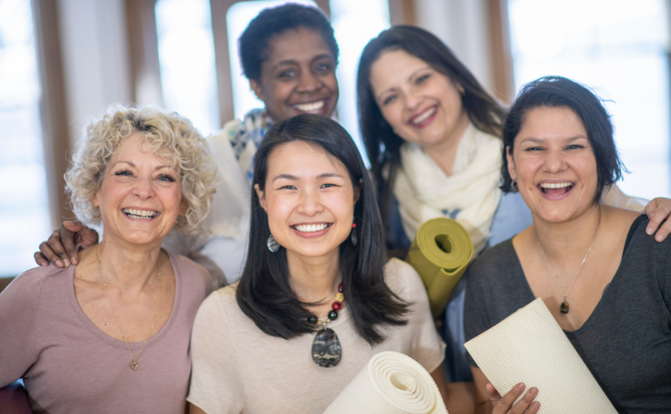 Group of 5 women smiling happily at camera and holding exercise mats